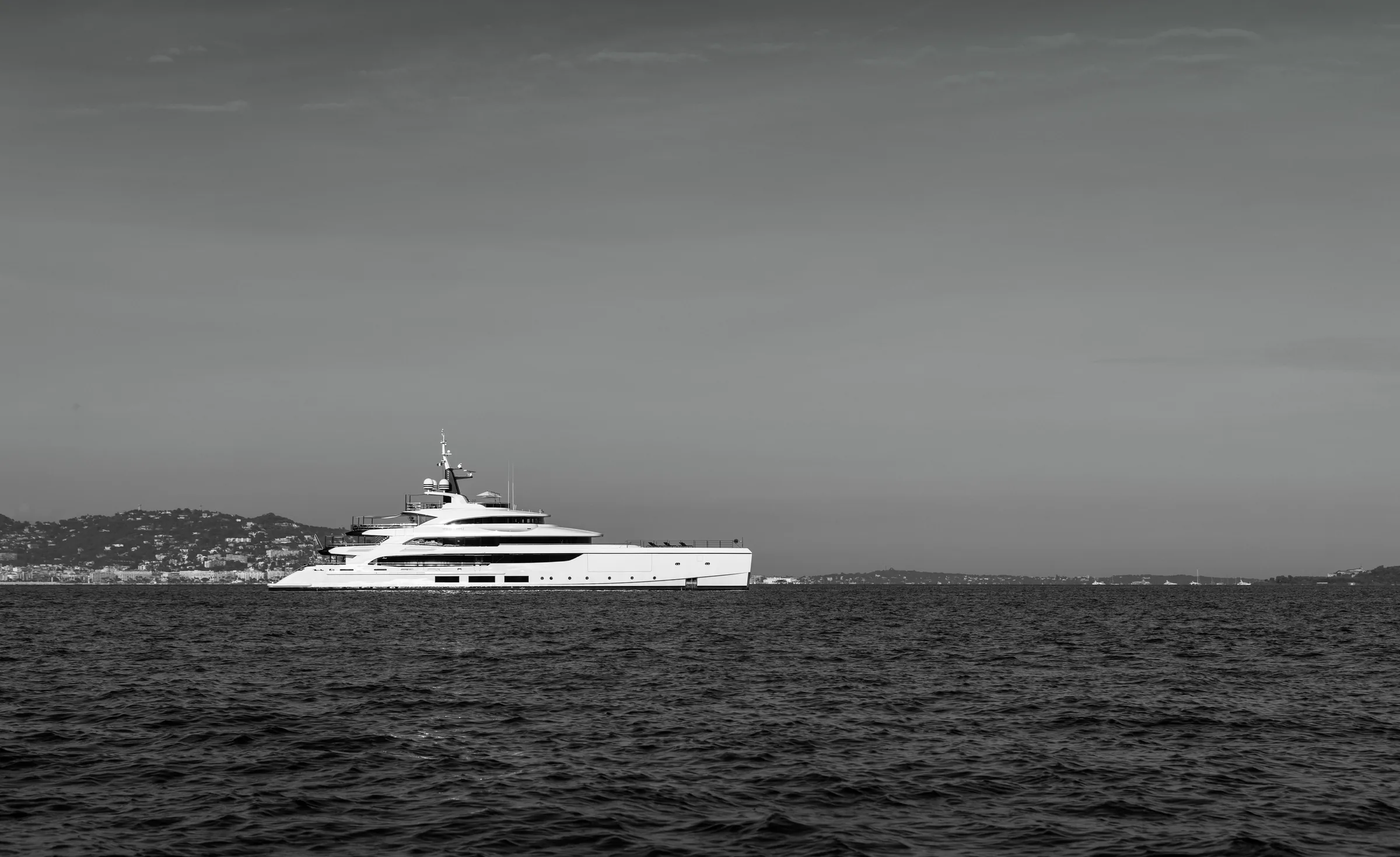 A yacht held off a pale coastline in flat grey weather, the horizon almost gone.