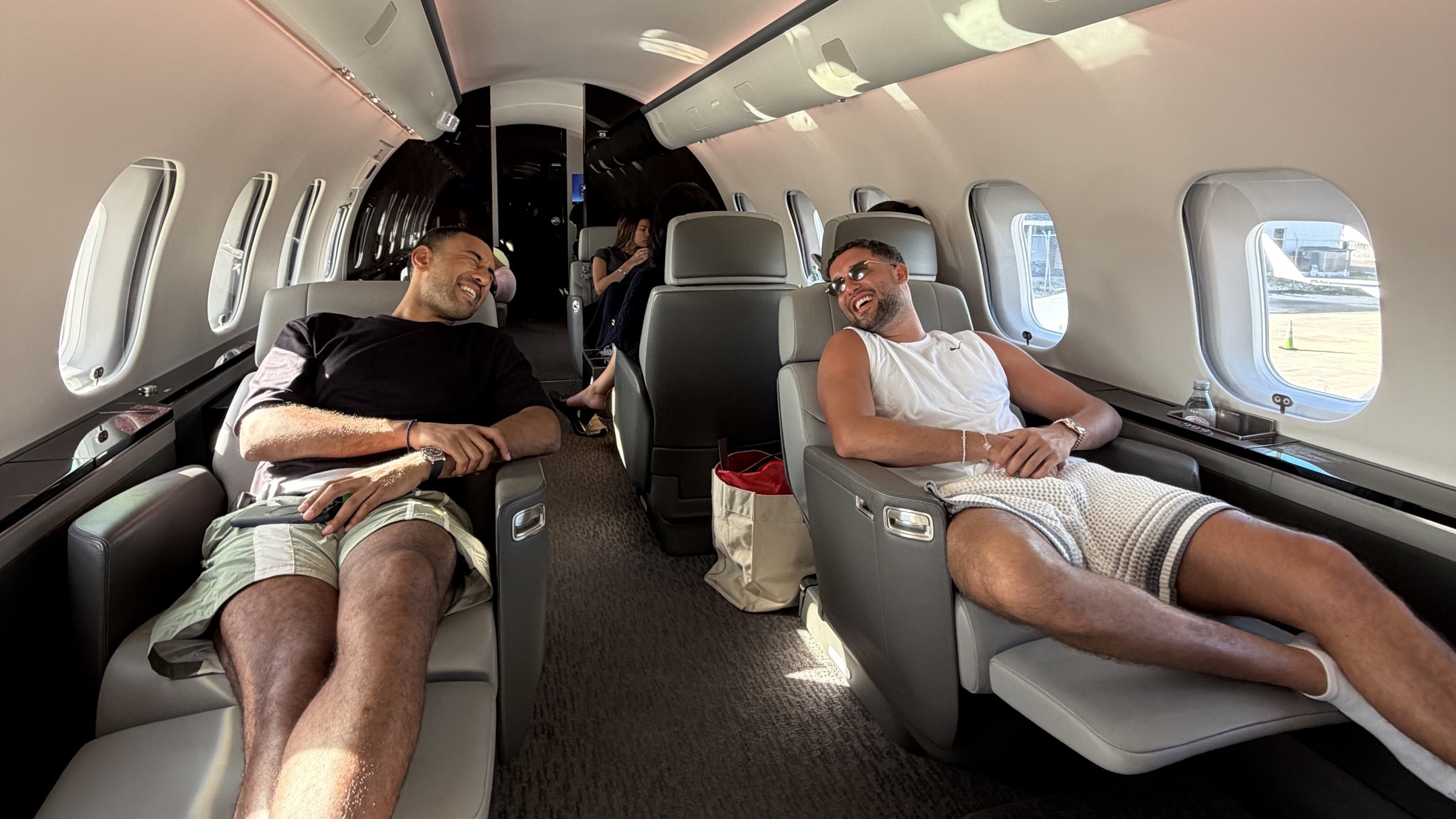 Two guests laughing across the aisle of a private jet, reclined in the sun.