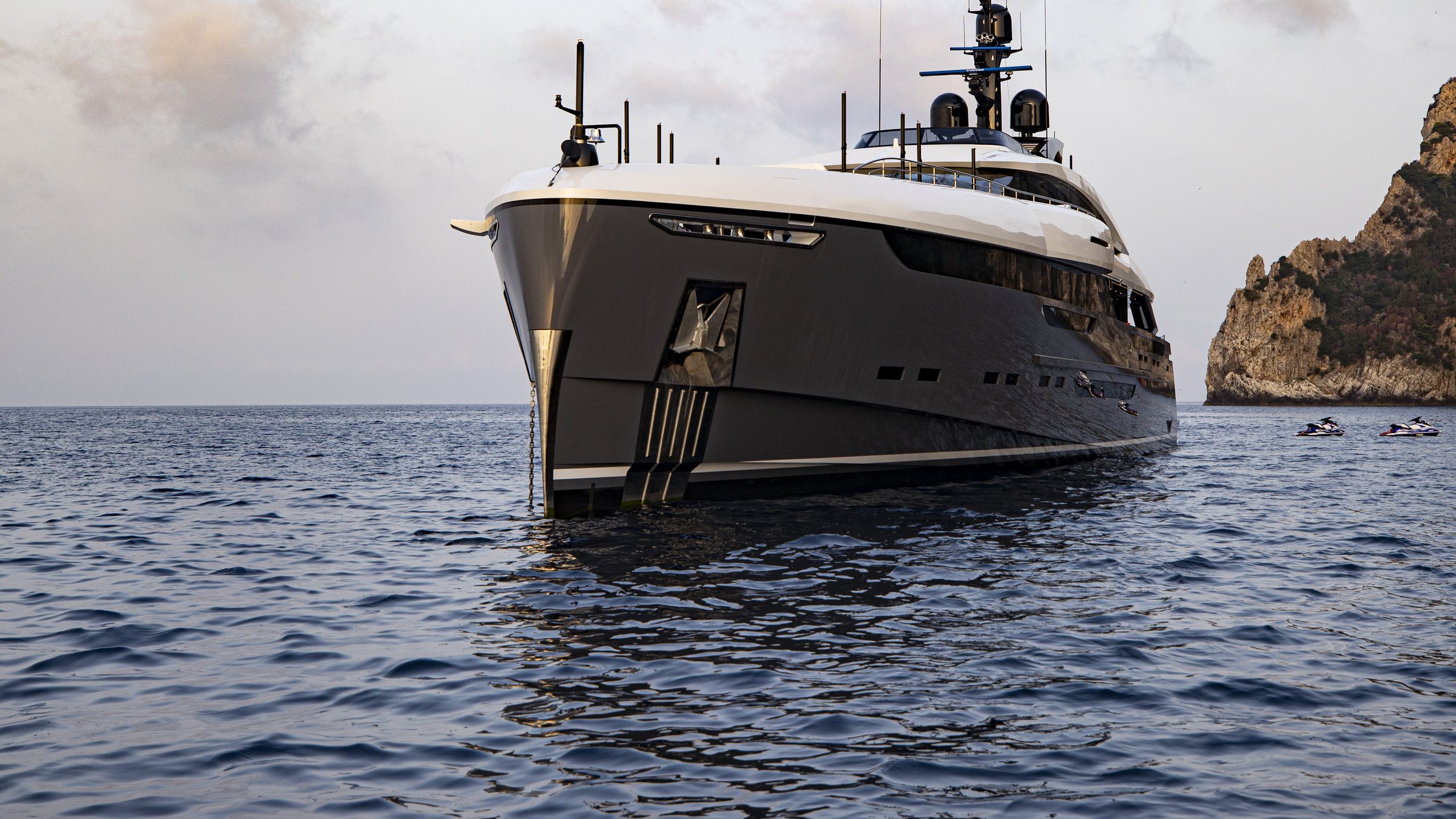 A superyacht at anchor, bow on, under a pale morning sky.