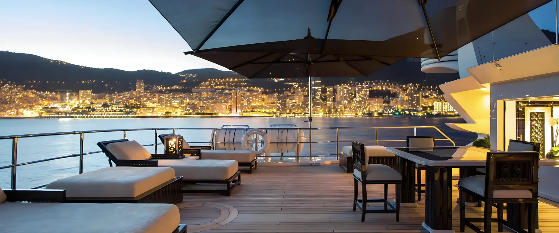 Monaco lit up at blue hour, seen across the water from a yacht's deck.