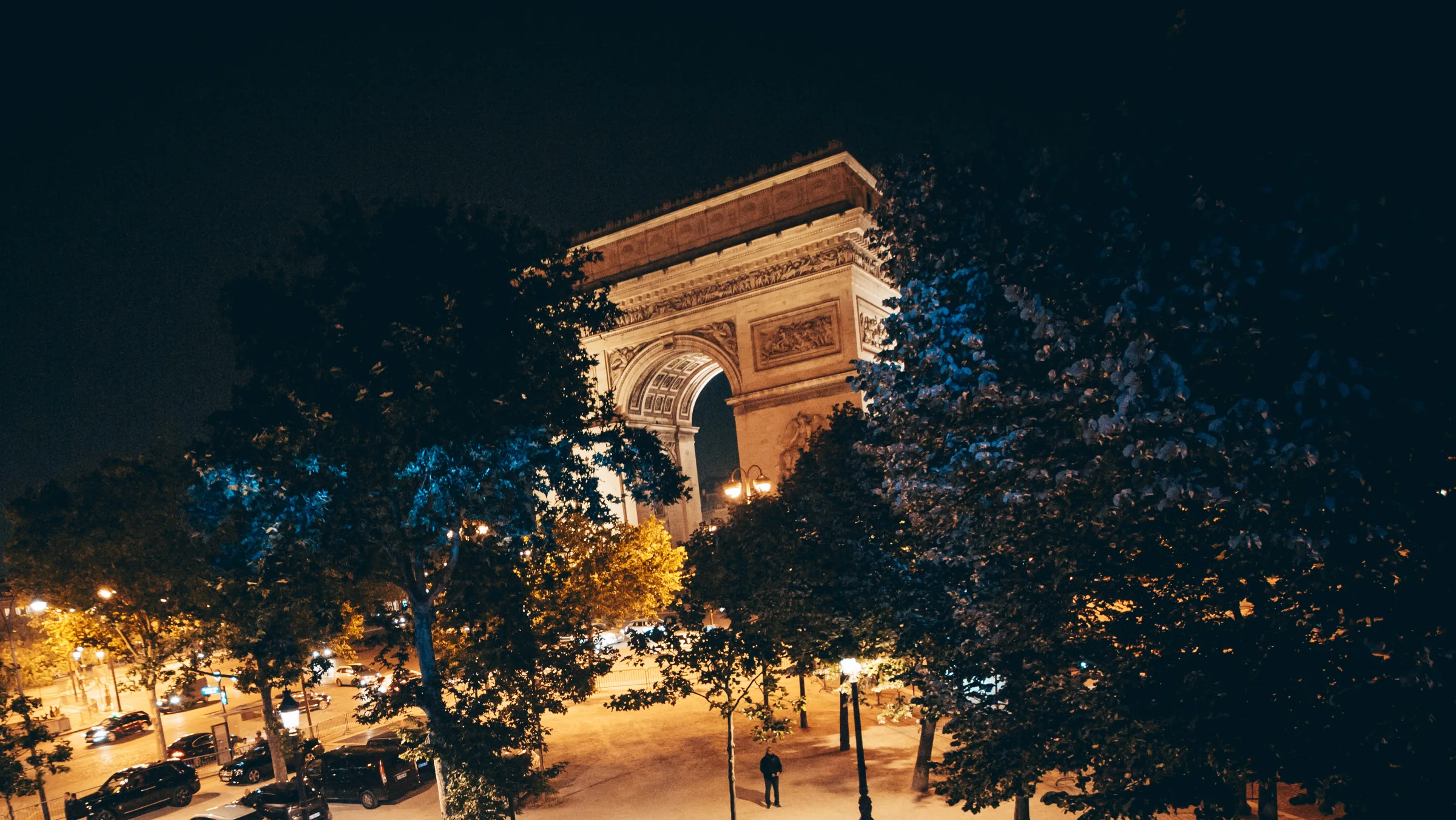 The Arc de Triomphe lit at night above the trees of the avenue, from L'Arc's terrace.